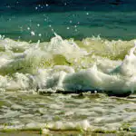 Bildnachweis 25 Brechende Welle an der Ostsee im Detail mit spritzender weißer Gischt, Wassertropfen und grünem Seegras.