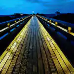 Bildnachweis 29 Beleuchtete Seebrücke aus Holz bei Heiligenhafen bei Nacht mit Spiegelung auf feuchten Planken unter blauem Himmel.