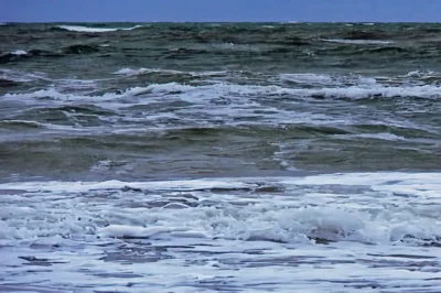 Stürmischer Wellengang auf der Ostsee mit dichten weißen Schaumkronen und Gischt unter grauem Himmel.